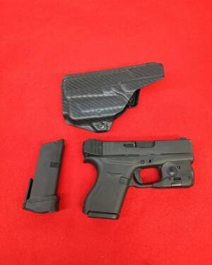 Used Glock 43 9mm Pistol with Streamlight TLR6 laser light and kydex holster on red background